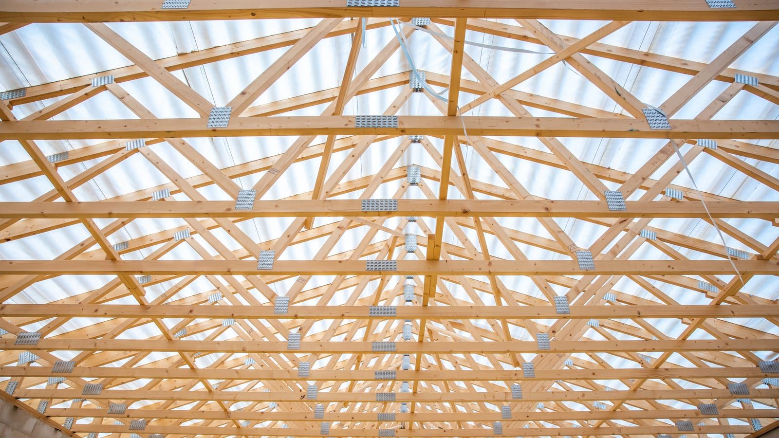 Cubierta de una nave en construcción con cerchas de madera bajo placas translúcidas, apoyada en muros de bloque de hormigón