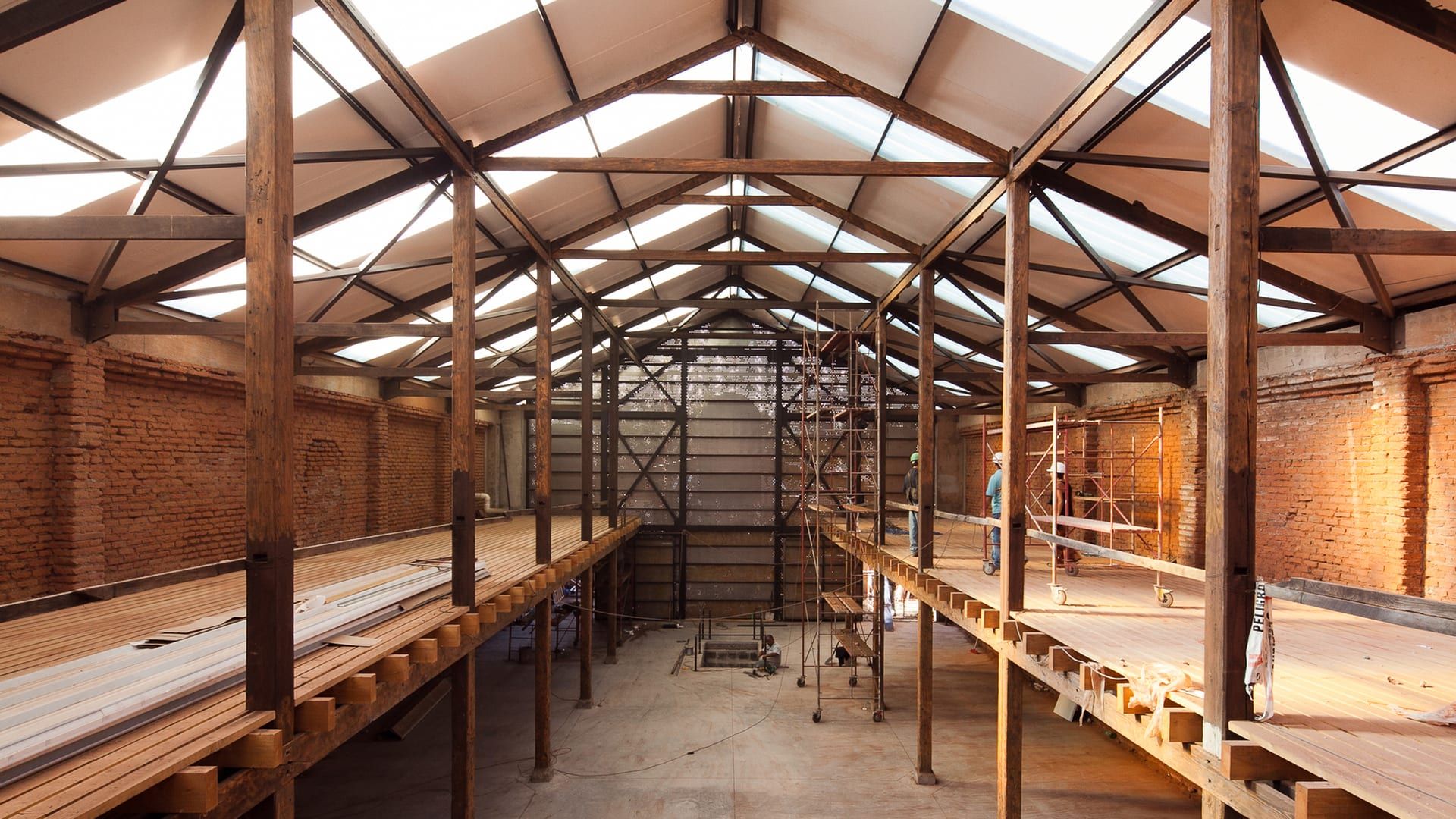 Interior de una nave con pilares y cerchas de madera, entreplantas laterales de madera y muros de ladrillo