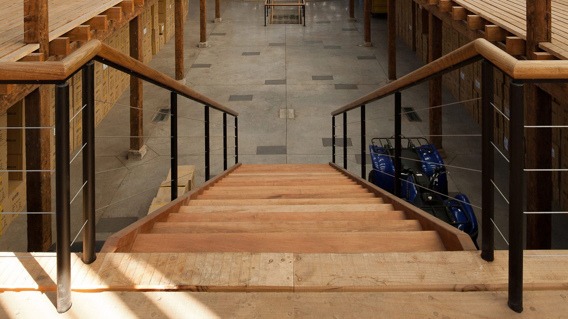 Interior de una nave con pilares, cerchas y entreplantas de madera, visto desde lo alto de una escalera